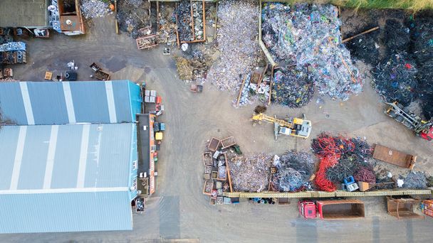 This image offers a detailed overhead look at the complex operations of a waste management facility. The scene is a mixture of order and disorder, with piles of recyclable materials segregated into - Photo, Image