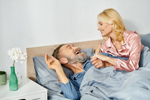 Um homem e uma mulher, um casal maduro e amoroso, em roupas de casa aconchegantes, pacificamente deitados na cama juntos, compartilhando um momento de intimidade e proximidade. - Foto, Imagem