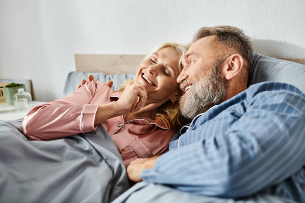 Kypsä mies ja nainen kodikas kotivaatteet makaa yhdessä sängyssä, jakaa rauhallinen hetki läheisyyttä ja yhteys. - Valokuva, kuva