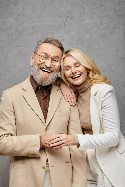 Een elegant, volwassen, liefdevol echtpaar in sierlijke kledij, naast elkaar staand tegen een grijze achtergrond. - Foto, afbeelding
