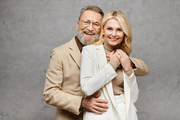 Un homme et une femme mûrs, exsudant l'élégance, posent ensemble dans une tenue élégante sur un fond gris. - Photo, image