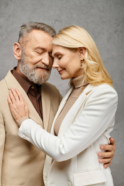 Debonair pareja con elegante atuendo compartiendo un cálido abrazo contra un sutil fondo gris. - Foto, imagen