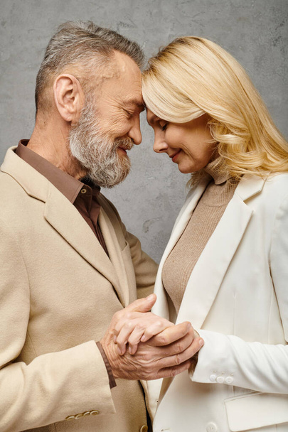 Взрослая любящая пара в облегающем одеянии, держащаяся за руки и улыбающаяся на сером фоне. - Фото, изображение