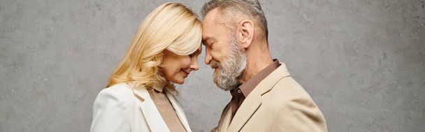 Un hombre y una mujer elegantes y maduros en atuendo debonair se unen contra un fondo gris. - Foto, Imagen