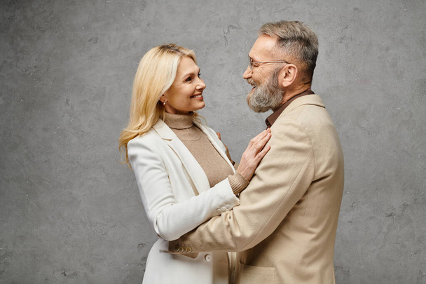 Elegante, volwassen man en vrouw in stijlvolle kledij rusten samen tegen een grijze achtergrond. - Foto, afbeelding