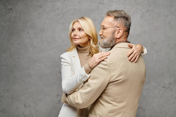 Взрослый мужчина и женщина, одетые элегантно, нежно обнимают друг друга на сером фоне. - Фото, изображение