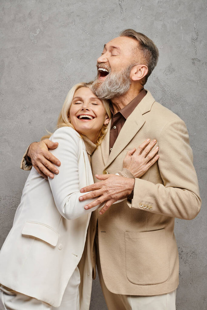 Un couple mature et élégant habillé en tenue débonnaire enveloppé d'une étreinte chaleureuse et aimante sur fond gris. - Photo, image