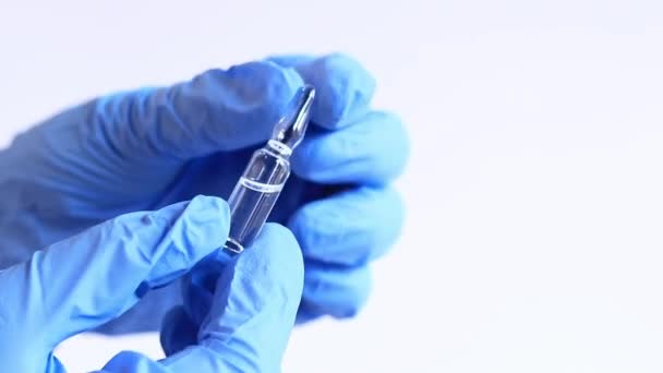Egy nő keze egy kék orvosi kesztyűben egy üvegampullát tart. Üvegampullák antibiotikumokkal vagy vakcinával, könnyű háttérrel. Egy orvos vagy nővér egy gyógyszert tart a kezében. - Felvétel, videó