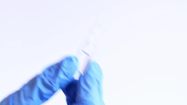 La main d'une femme dans un gant médical bleu tient une ampoule en verre. Ampoules en verre avec antibiotiques ou vaccin sur fond clair. Un médecin ou une infirmière tient un médicament en main - Séquence, vidéo