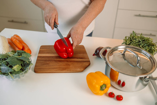 Zamknij przycięty obraz cięcia deski i kobieta cięcia warzyw papryki w kuchni, przygotowując posiłek w domu. Wegetariańskie zdrowe jedzenie. Wysokiej jakości zdjęcie - Zdjęcie, obraz