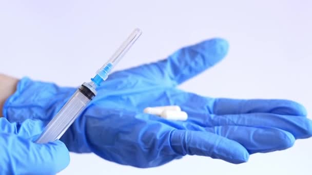 Injectie of pil. De arts houdt een spuit en een pil vast. Handen in blauwe handschoenen met een spuit en capsule. Verschillende soorten behandelingen - Video