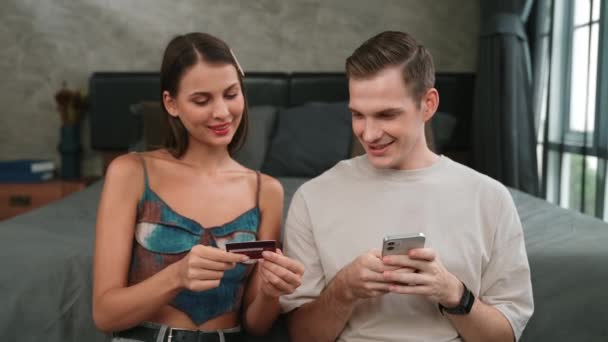 Молода пара сидить у домашній спальні, використовуючи онлайн-додаток оплати та цифровий гаманець на смартфоні для оплати кредитною карткою. Купівля електронної комерції та сучасні покупки через мобільний інтернет. Адіт - Кадри, відео