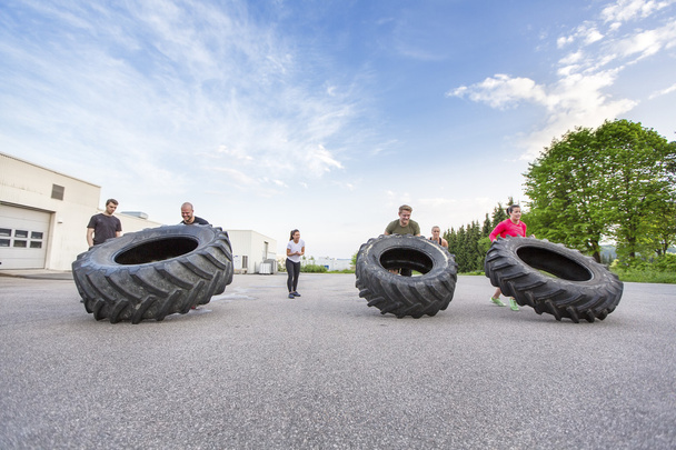 Тренировочная команда подбрасывает тяжелые шины на открытом воздухе
 - Фото, изображение