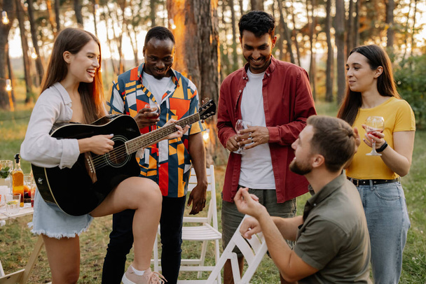 Aantrekkelijke hipster vrouw spelen gitaar winnen voor mannen op diner feest met multiraciale vrienden - Foto, afbeelding