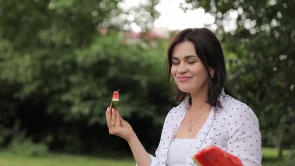 Uma mulher segura uma melancia na mão, desfrutando de um momento de lazer entre grama e árvores, com uma expressão feliz. - Filmagem, Vídeo