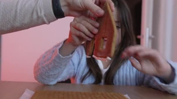 Маленькая девочка помещает кусочек пряничного домика. Крупный план ребенка, занимающегося творческими праздниками - Кадры, видео