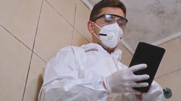 καθαρισμός καλουπιών, μουχλιασμένο μπάνιο και ένας άνθρωπος σε μια επαγγελματική στολή προστασίας ψεκάζοντας χημικά για να σκοτώσει μούχλα και μούχλα - Πλάνα, βίντεο