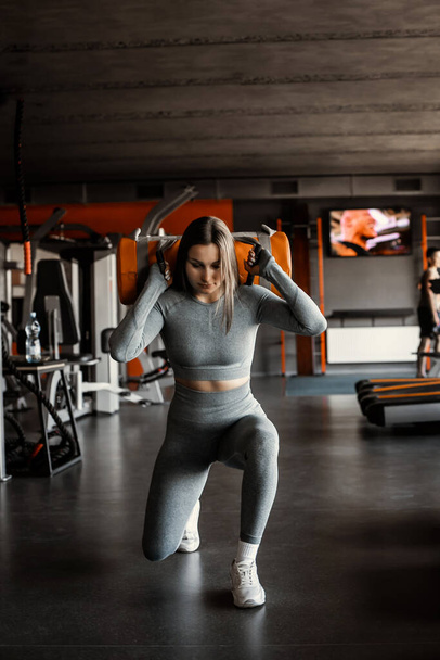 Sporty young woman in grey rash guard working out with sandbag while exercises in the gym. Attractive athletic female doing hard workout with weight training with copy space for your text message. - Valokuva, kuva