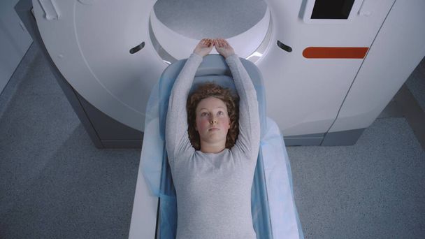 Close-up van een vrouwelijke patiënt liggend op CT, PET, of MRI scan bed, bewegend in de machine. High-tech apparatuur scant lichaam en hersenen van patiënten in een medische faciliteit met geavanceerde technologieën. - Foto, afbeelding