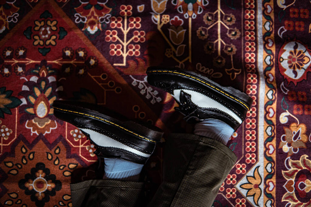 Close-up van tweekleurige vleugeltip brogue schoenen gemaakt van echt leer binnenshuis gedragen op de klassieke rode loper. Concept foto van klassieke vleugeltip brogue schoenen met een rode Turkse tapijtbodem - Foto, afbeelding