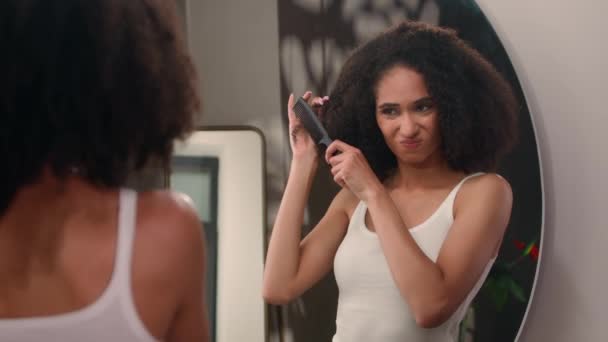 Frustrado exausto louco raiva triste afro-americano mulher tentando pentear cachos sofrem com problema de cuidados com o cabelo olhando espelho reflexão menina sofrimento feminino tentar escova encaracolado emaranhado cabelo no banheiro - Filmagem, Vídeo