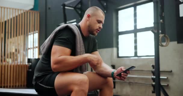 Athlete, man and phone in gym for break with sweating, relax and tired of exercise, workout and training. Bodybuilder, person and smartphone for communication, text message or fitness progress on app. - Footage, Video