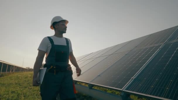 Een mannelijke arbeider met documentatie voert taken uit op een zonnepaneelstation. Toezicht op de werking van het elektriciteitsopwekkingssysteem. Groene elektriciteit concept. Hoge kwaliteit 4K beeldmateriaal - Video