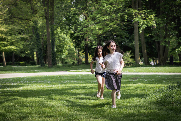 Twee mooie Kaukasische brunette meisjes spelen gelukkig terwijl lopen inhalen op een zomerse dag in een openbaar park, close-up side view. - Foto, afbeelding