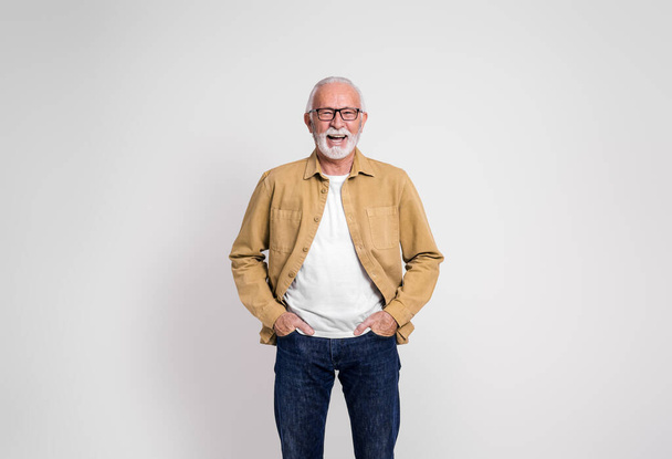 Πορτρέτο του χαρούμενου ηλικιωμένου επιχειρηματία με τα χέρια στις τσέπες γελώντας σε απομονωμένο λευκό φόντο - Φωτογραφία, εικόνα