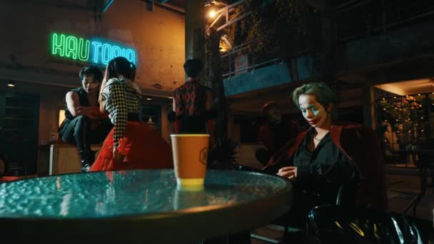 Стильные молодые люди сидят в тускло освещенном городском кафе с неоновыми вывесками, излучая прохладную, современную атмосферу в ночное время - Кадры, видео