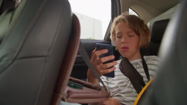 Niño de 12 años enfocado en su smartphone en el asiento trasero - Metraje, vídeo