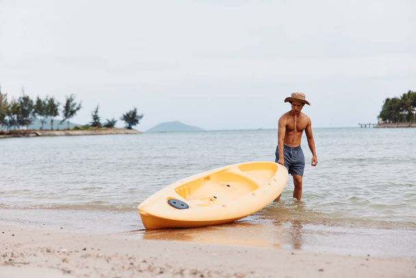 Щасливий азіатський чоловік Кейкінг на тропічному пляжі: вражаюча пригода водного спорту серед пальмових дерев та бірюзового океану - Фото, зображення