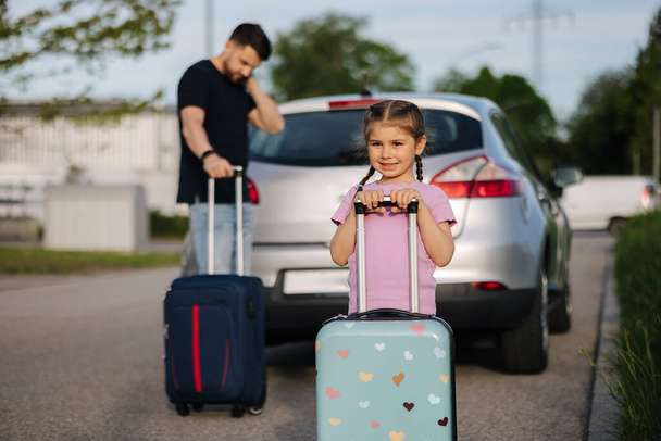 Baba ve kızı bavullarıyla açık bagajlı bir arabanın yanında duruyorlar. Küçük mutlu kız seyahate hazırlanıyor. Yüksek kalite fotoğraf - Fotoğraf, Görsel