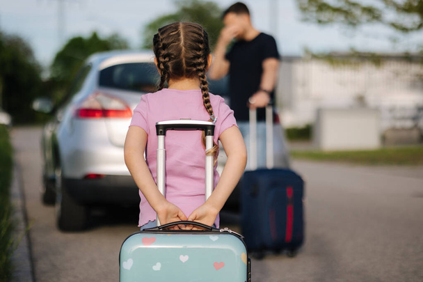 Vater und Tochter stehen mit ihren Koffern neben einem Auto mit offenem Kofferraum. Glückliches kleines Mädchen bereitet sich auf die Reise vor. Hochwertiges Foto - Foto, Bild