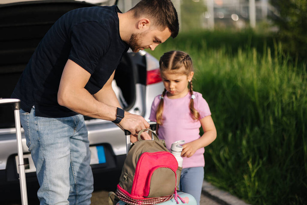 Baba ve kızı bavullarıyla açık bagajlı bir arabanın yanında duruyorlar. Küçük mutlu kız seyahate hazırlanıyor. Yüksek kalite fotoğraf - Fotoğraf, Görsel