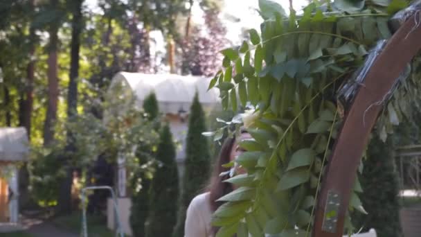 Professional florist worker decorates festive arch for ceremonial marriage registration. Woman Installing wedding decor. Decorator decorate arch outdoor wedding ceremony with flowers and greenery. - Footage, Video