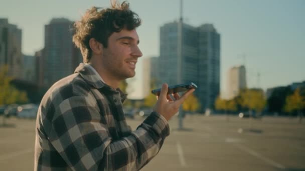 Ευτυχισμένος Καυκάσιος άντρας ηχογραφεί φωνητικό μήνυμα σε smartphone περπατώντας δρόμο της πόλης χαμογελαστός τύπος κουβεντιάζοντας με φίλους στο κινητό τηλέφωνο online messenger ηχογράφηση ηχητικό μήνυμα με ηχείο μεγάφωνο - Πλάνα, βίντεο