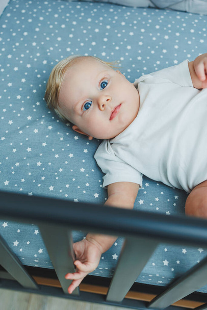 Photo d'un bébé de 5 mois couché dans un berceau. Un lit bébé avec un petit garçon en body blanc. - Photo, image