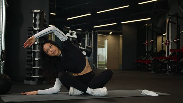 Fit slim Καυκάσια αθλήτρια αθλητική υγιή ενεργό γυναίκα τεντώσει τους μυς του σώματος προπόνηση πλευρά κάμψη κάμψη άσκηση σε λωτό θέση σπορ κορίτσι γυμναστής γυμναστικής τεντώνοντας γιόγκα αθλητισμού προπόνηση στο γυμναστήριο - Φωτογραφία, εικόνα