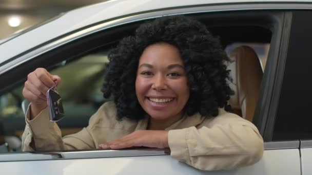 Cliente comprador femenino afroamericano feliz de la muchacha en coche nuevo que muestra la llave del automóvil de lujo alegre mujer sonriente del negocio que compra el transporte compra auto eléctrico en tienda del salón de la concesionaria del vehículo - Imágenes, Vídeo