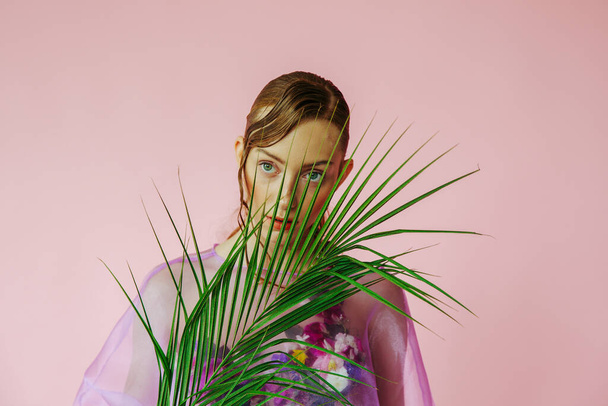 young beautiful woman posing with palm leaf in pink dress over pink background - Valokuva, kuva