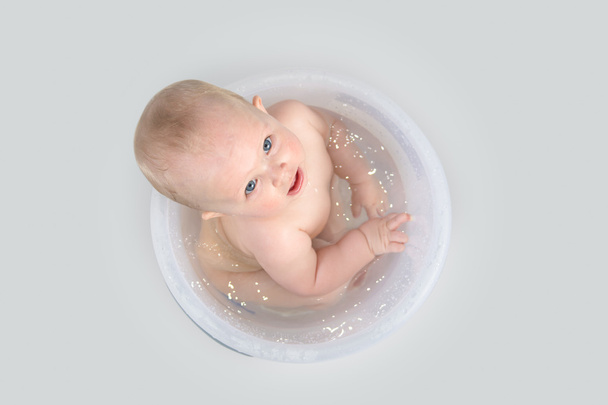 Милый ребенок принимает ванну в прозрачном ведре и играет с игрушками
 - Фото, изображение