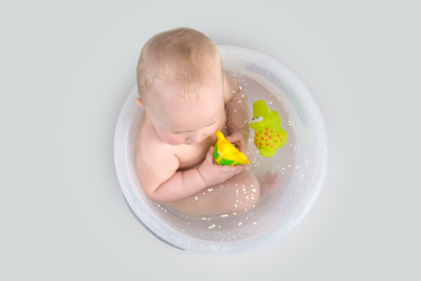 niedliches Baby mit einem Bad im transparenten Eimer und Spielen mit Spielzeug - Foto, Bild