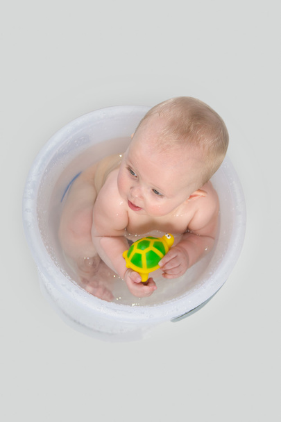 Schattige Baby met een bad In transparante emmer en spelen met speelgoed - Foto, afbeelding