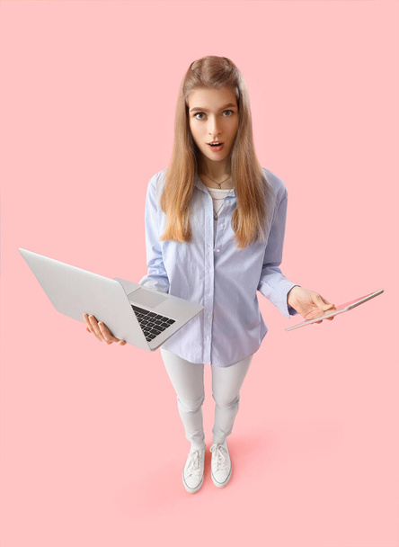 Шокована жінка-програмістка з ноутбуком і планшетним комп'ютером на рожевому фоні - Фото, зображення