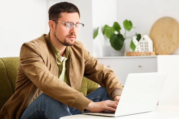Schöner Mann mit stylischer Brille mit Laptop zu Hause - Foto, Bild