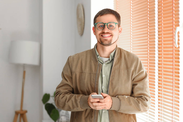 Komea mies tyylikkäissä silmälaseissa matkapuhelimen avulla kotona - Valokuva, kuva