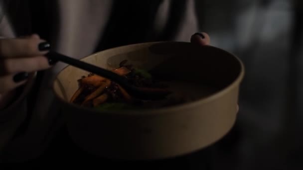 Vrouwen handen houden een bord met gezond voedsel vast. Onherkenbare vrouw die 's nachts eet van een kartonnen bord en plastic vork in een café in de stad - Video