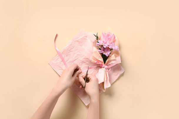 Žena dělat kytici krásných jarních květin v balení papíru na béžové pozadí. Mezinárodní den žen - Fotografie, Obrázek