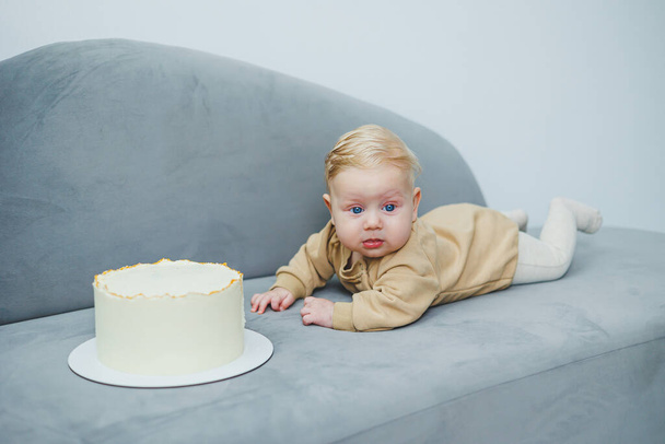 Malý čtyřměsíční chlapec se plazí k sladkému dortu. Novorozený chlapec v béžovém obleku se plazí po pohovce k dortu. - Fotografie, Obrázek